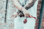Stylish tattooed individual showcasing rock style fashion near urban brick wall.