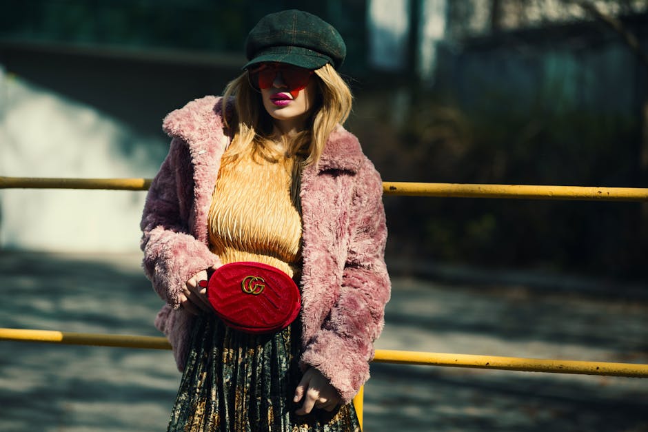 Fashionable woman in a pink coat posing outdoors with a trendy red bag and cap.