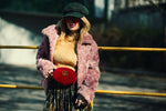 Fashionable woman in a pink coat posing outdoors with a trendy red bag and cap.
